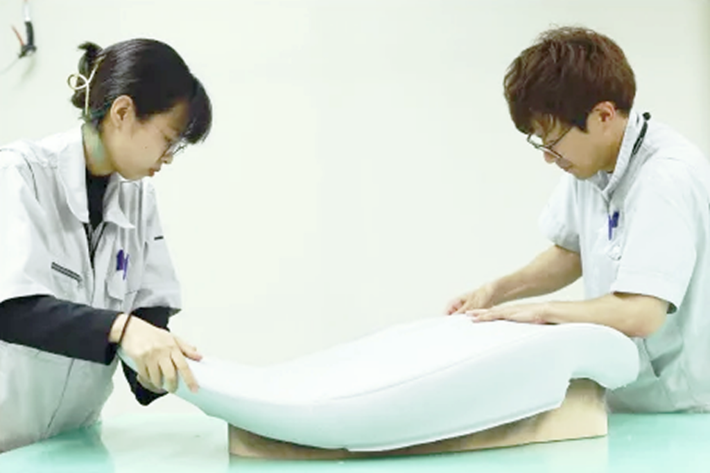 Two clinicians in white coats fit a curved white leg immobilizer around a patient’s leg on a treatment table.