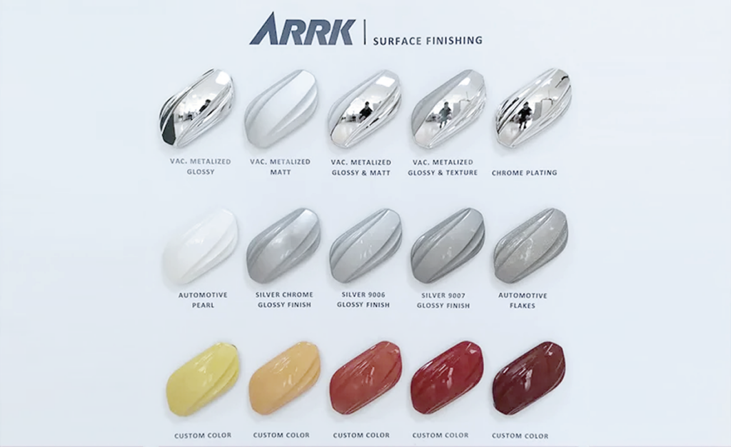 Swatch board by ARRK Surface Finishing showing multiple color and finish samples (metalized gloss/matt, chrome, automotive pearls, and custom colors) arranged in rows with captions beneath each swatch.